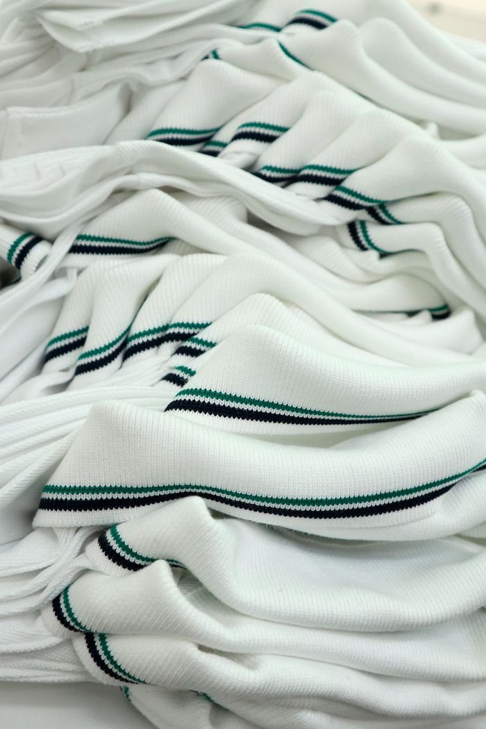 Servicios Pile of white knit fabric with black and green stripes, ideal for fashion projects.